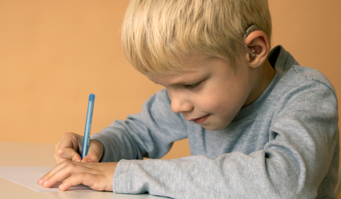 Foto But mit Hörhilfe schreibt an einem Pult.