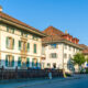 Gebäude der Gemeindeverwaltung von Münchenbuchsee im Jahr 2018. Mehrere traditionelle Verwaltungsgebäude mit Ziegeldach und Fensterläden stehen an einer ruhigen Strasse unter blauem Himmel.